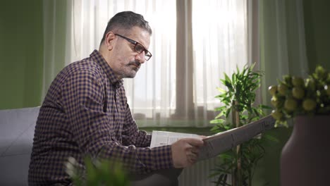 Middle-aged-man-in-glasses-reading-newspaper-at-home,-enjoying-his-free-time.